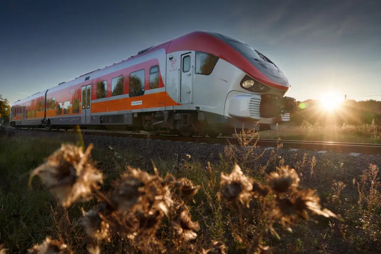 Nowoczesny pociąg Polregio na trasie Rzeszów - Ustrzyki Dolne, sunący przez malownicze tereny o zachodzie słońca.