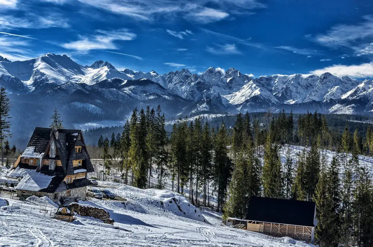 Zimowe Tatry zachwycają. Drewniane domy i lasy otaczają ośnieżone szczyty. Idealne miejsce na szlaki zimowe Tatry.