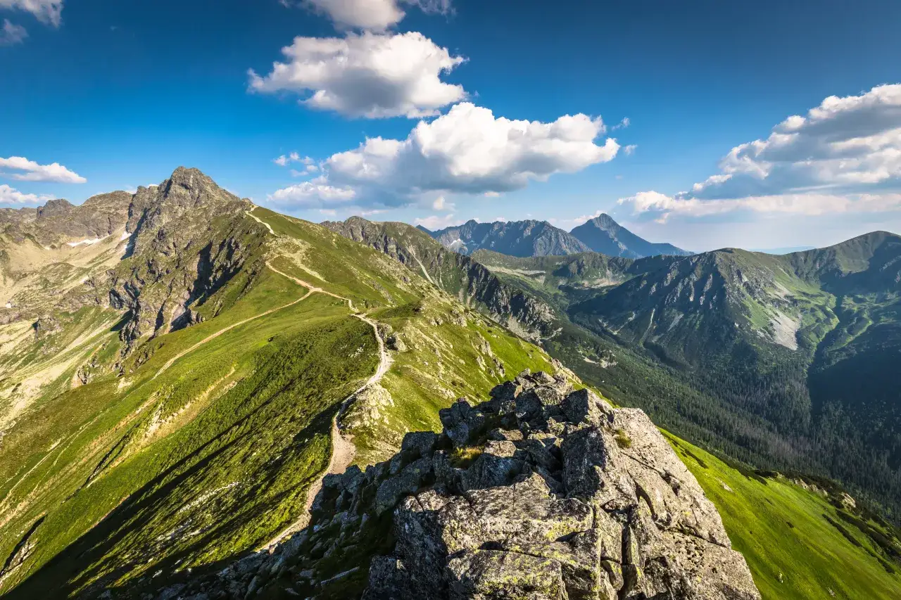 Niebieski szlak na Giewont wije się po zielonych zboczach Tatr, prowadząc przez skaliste i trawiaste tereny.