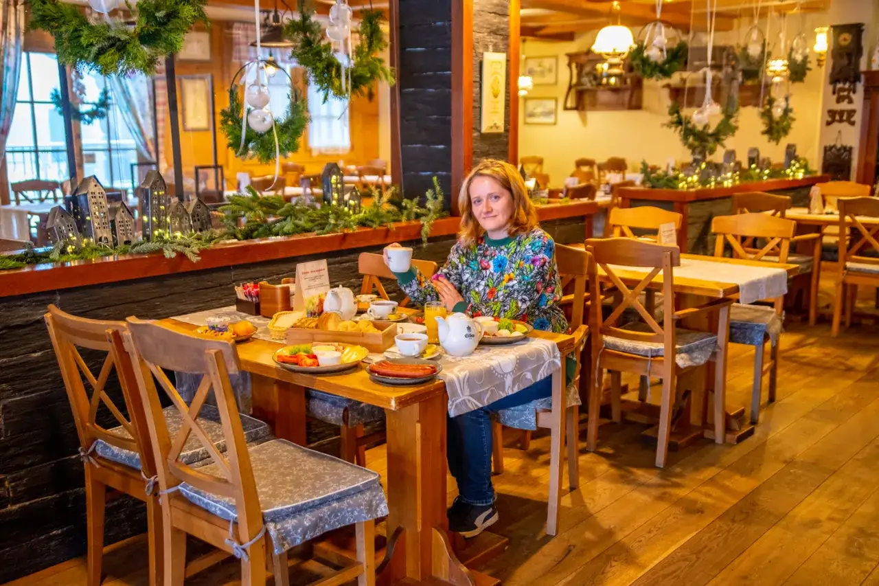Kobieta pije kawę przy stole z obfitym śniadaniem w przytulnej restauracji. Idealne miejsce, gdzie zjeść w Chochołowie.