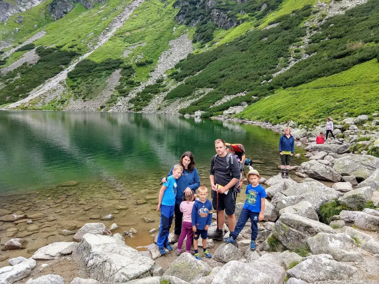 Rodzina odpoczywa nad jeziorem u podnóża Kasprowego Wierchu, w tle zielone zbocza i hala gąsienicowa.