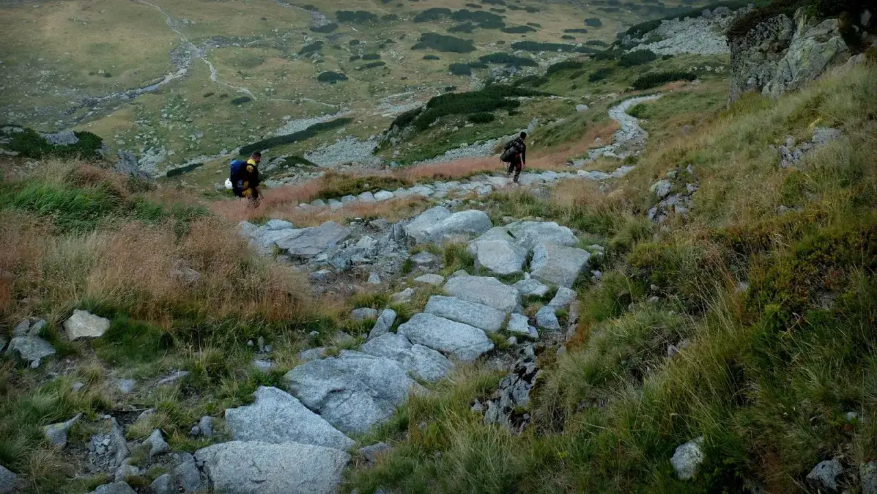 Dwóch turystów z plecakami schodzi kamienistym szlakiem. Piękne widoki na Tatry podczas wycieczki.