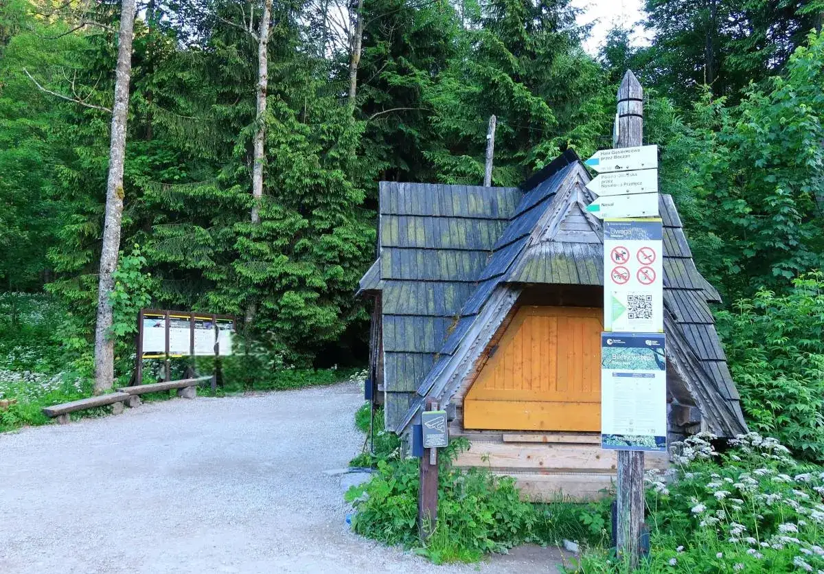 Drewniana chata przy szlaku w Dolinie Jaworzynki. Znaki kierunkowe wskazują drogę, a tablice informują o zasadach panujących w okolicy.