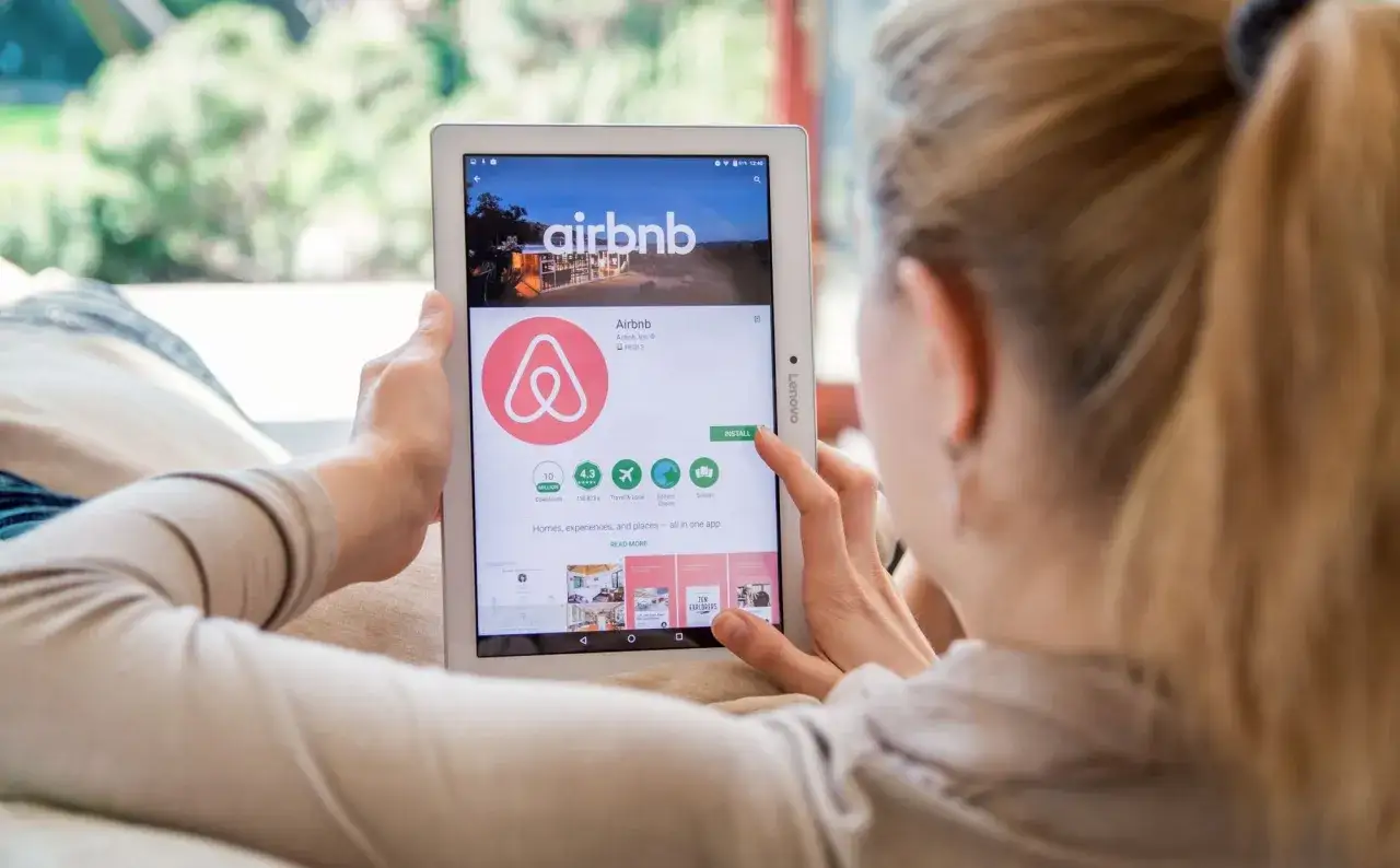 Kobieta przegląda aplikację Airbnb na tablecie, szukając inspiracji, gdzie najlepiej rezerwować noclegi.