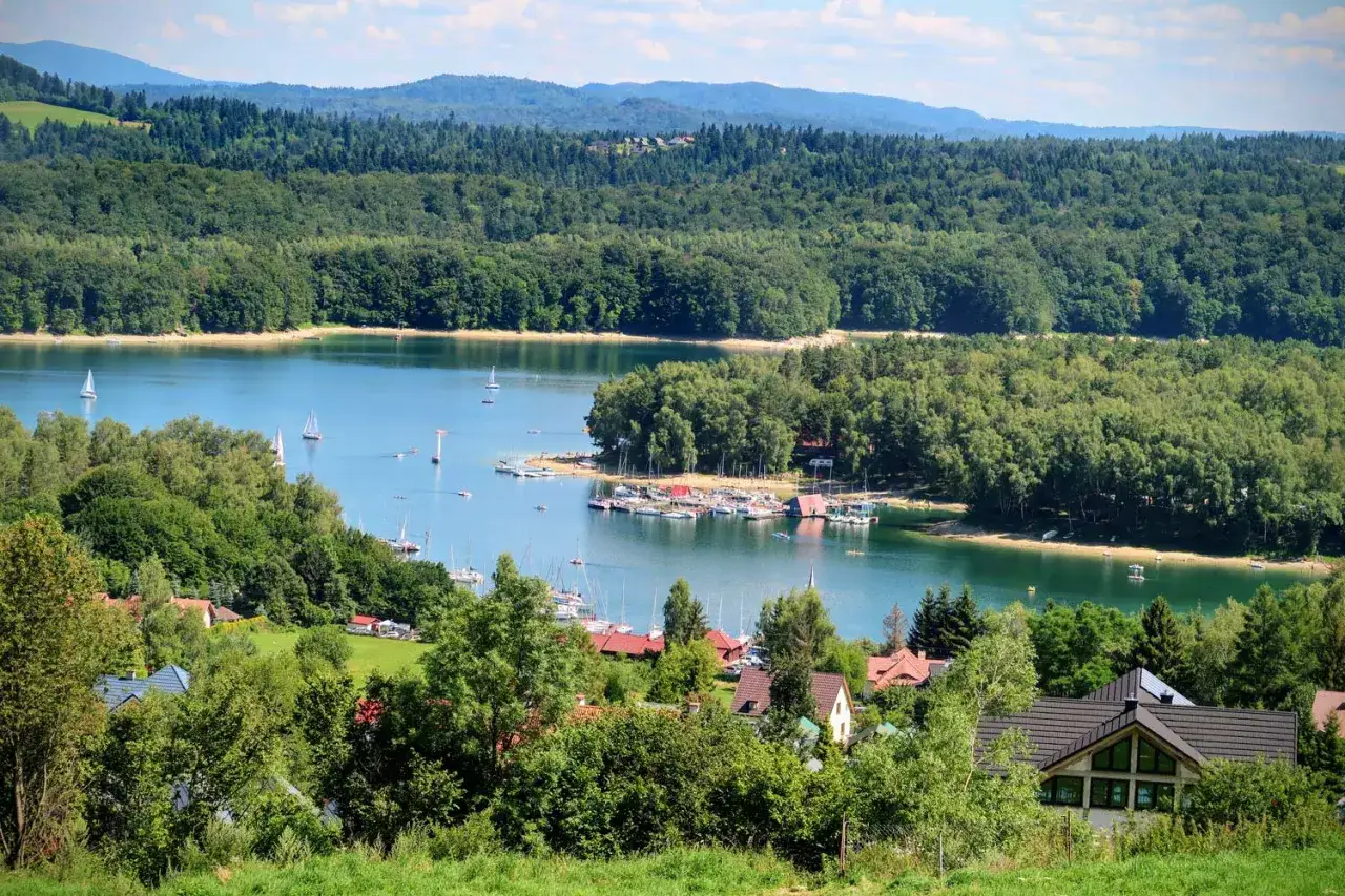 Malowniczy widok na plażę nad Soliną, z żaglówkami na wodzie i zielonymi wzgórzami w tle.