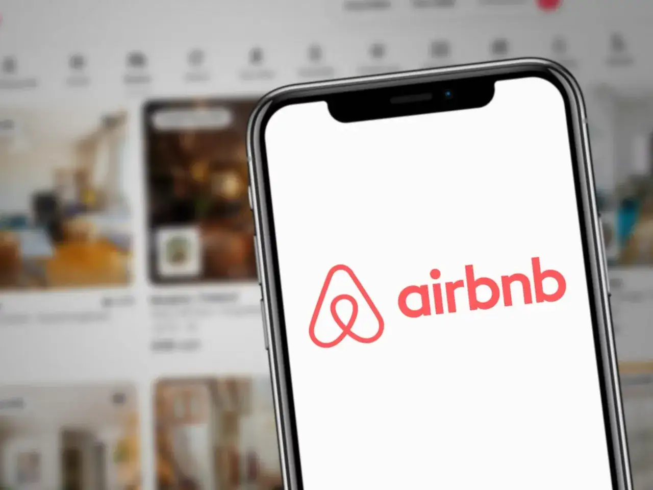 Telefon z logo Airbnb, idealne miejsce, gdzie najlepiej rezerwować noclegi. W tle widać oferty mieszkań.
