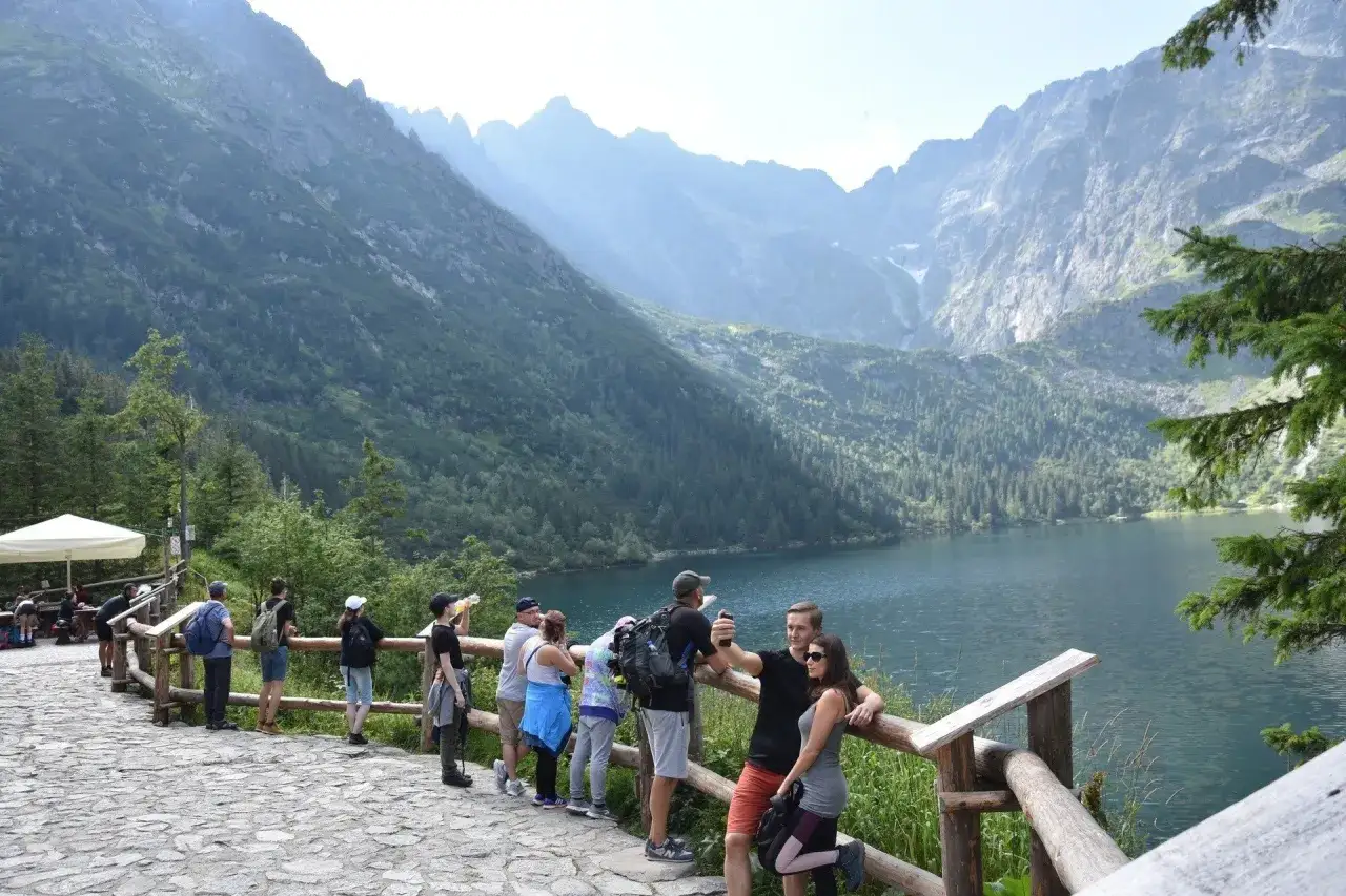 Grupa turystów podziwia malowniczą drogę nad Morskie Oko, robiąc zdjęcia na tle gór i jeziora.