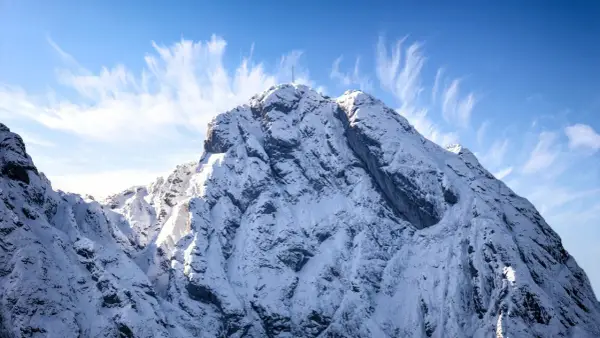 Ośnieżony szczyt Giewontu z krzyżem, pod błękitnym niebem z pierzastymi chmurami. Zastanawiasz się, ile trwa wejście na Giewont?