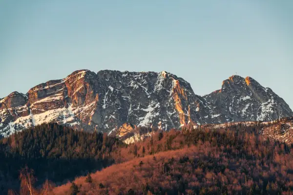 Giewont ośnieżony, z krzyżem na szczycie, w złotym świetle zachodzącego słońca. Czy ciężko wejść na Giewont? Widok zapiera dech w piersiach.